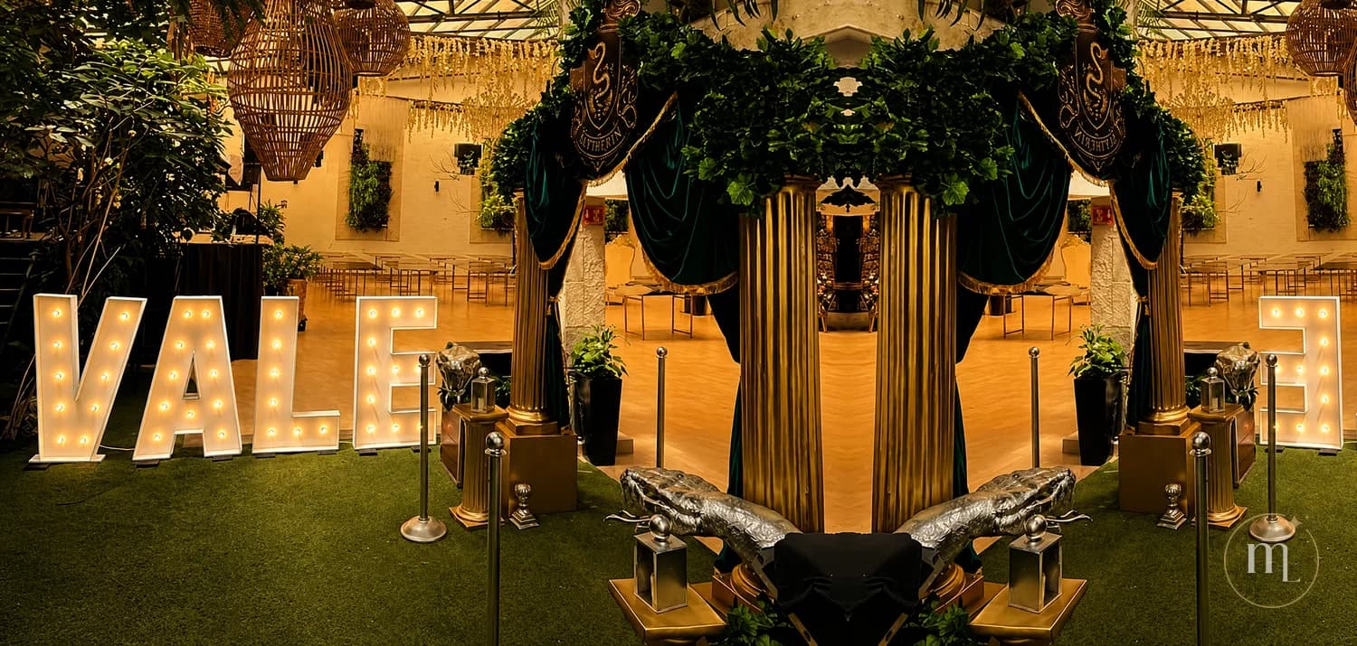 El nombre VALE en letras iluminadas sobre el pasto de un salón, entre plantas y faroles