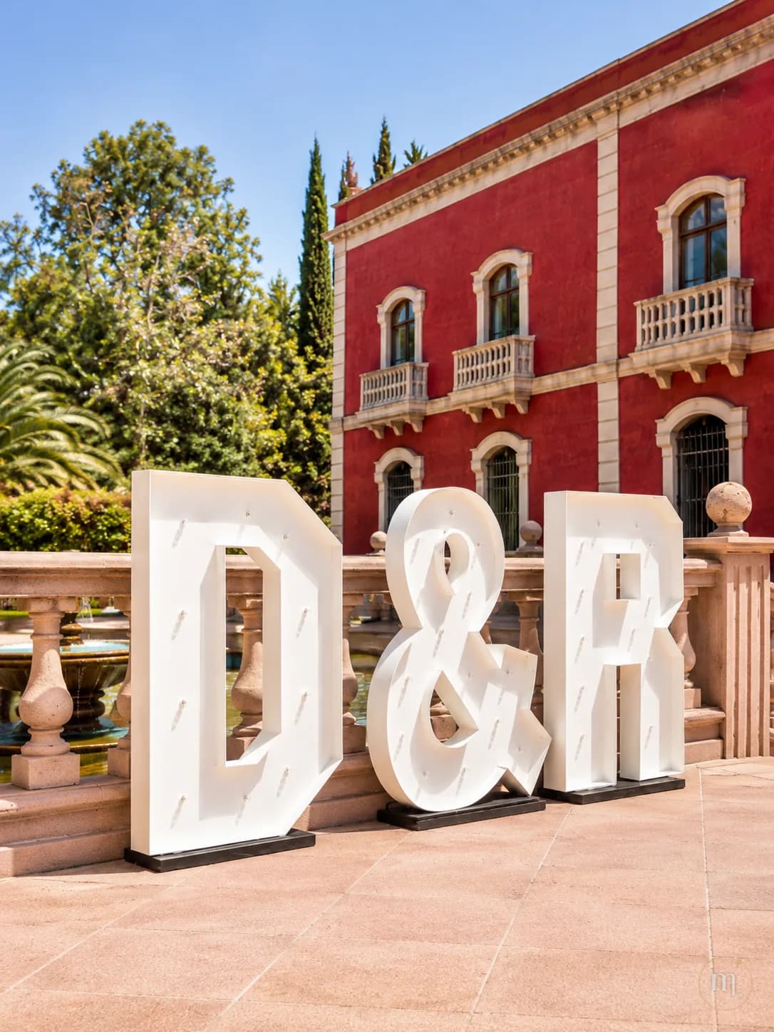 Las iniciales D y R con un ampersand, montadas frente a una hacienda