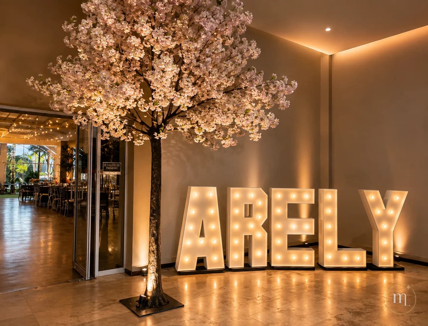 El nombre ARELY en letras iluminadas junto a un árbol de flores de cerezo, reflejándose en el piso de mármol de un salón