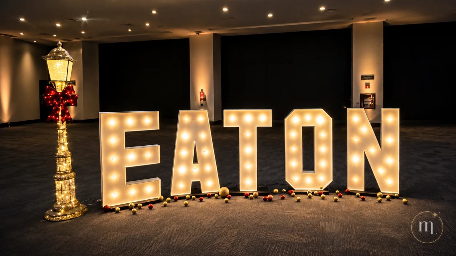El nombre EATON en letras iluminadas dentro de un salón, junto a un farol y esferas doradas y rojas