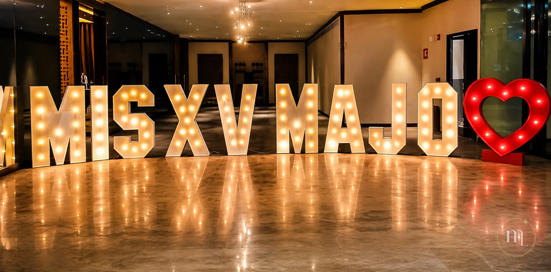 MIS XV MAJO en letras iluminadas con el corazón rojo al lado, reflejándose en el piso de mármol de un vestíbulo