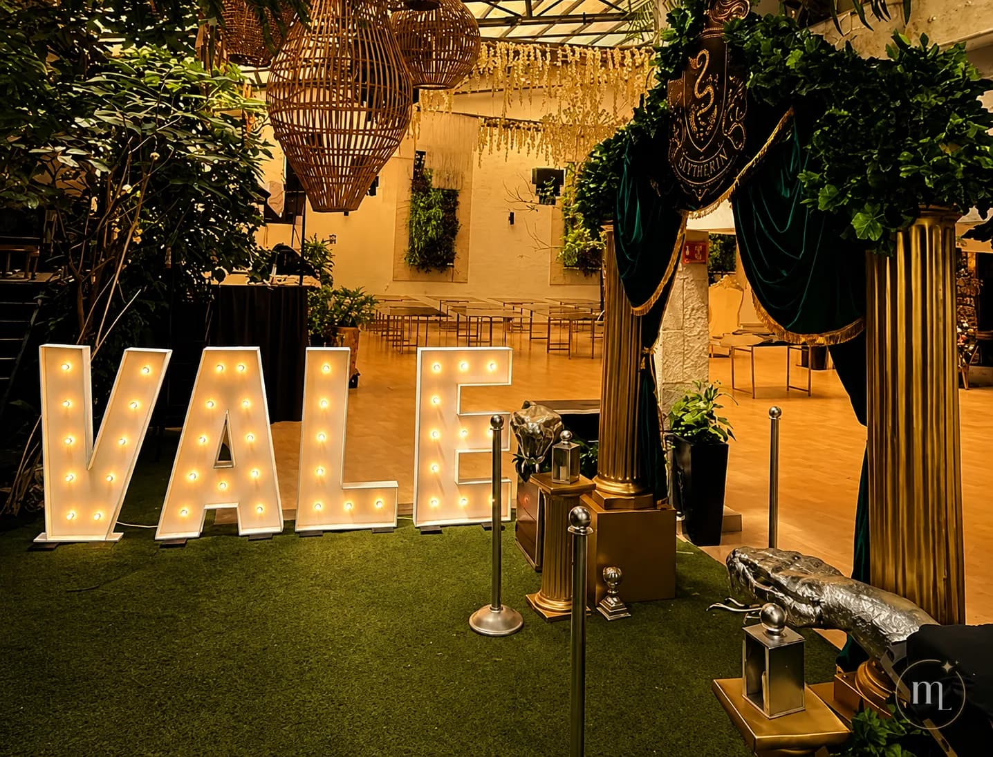 El nombre VALE en letras iluminadas sobre el pasto de un salón, entre plantas y faroles